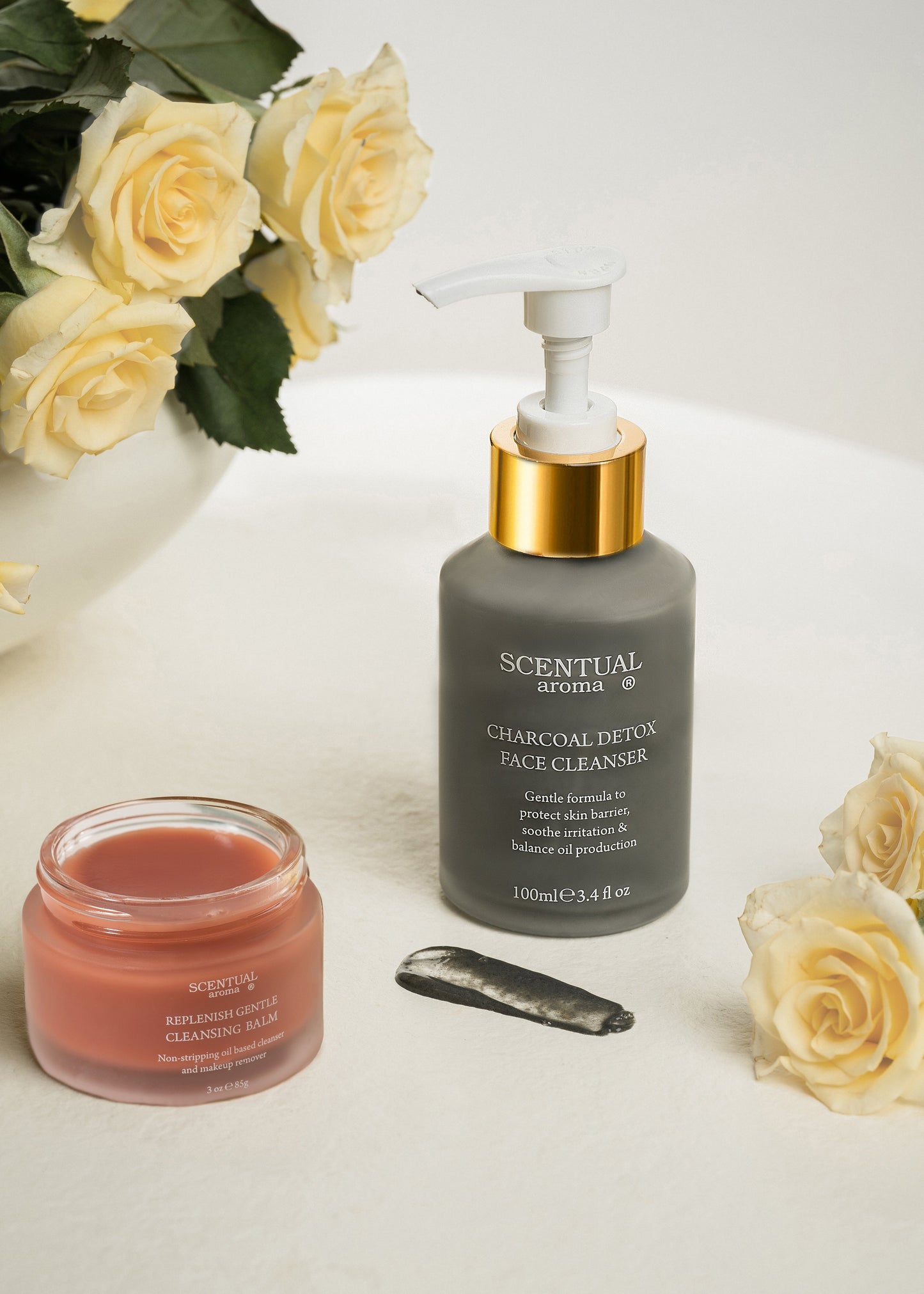 Scentual Aroma Charcoal Detox Face Cleanser and Replenish Gentle Cleansing Balm jar on a white surface with yellow roses.
